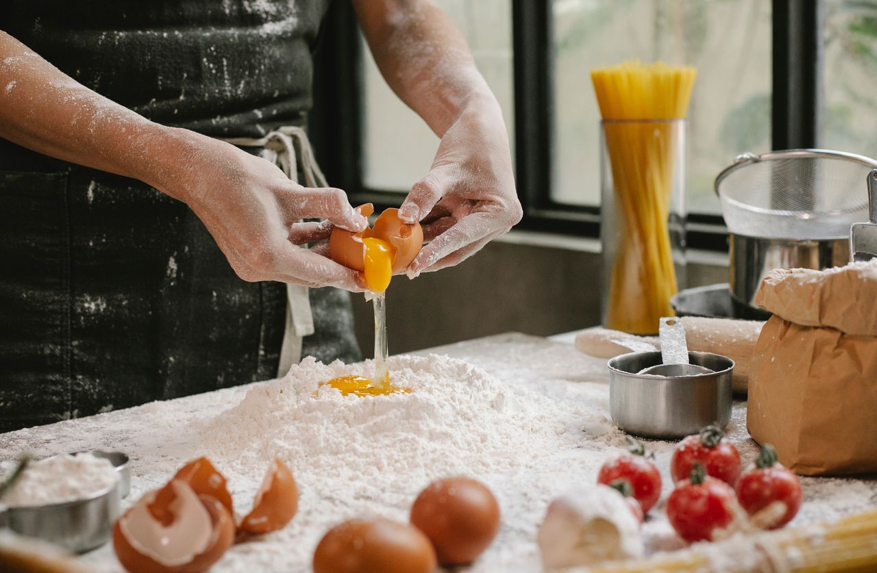 creative-approach-img Crop anonymous person adding egg in flour while cooking pastry for recipe with cherry tomatoes and spaghetti