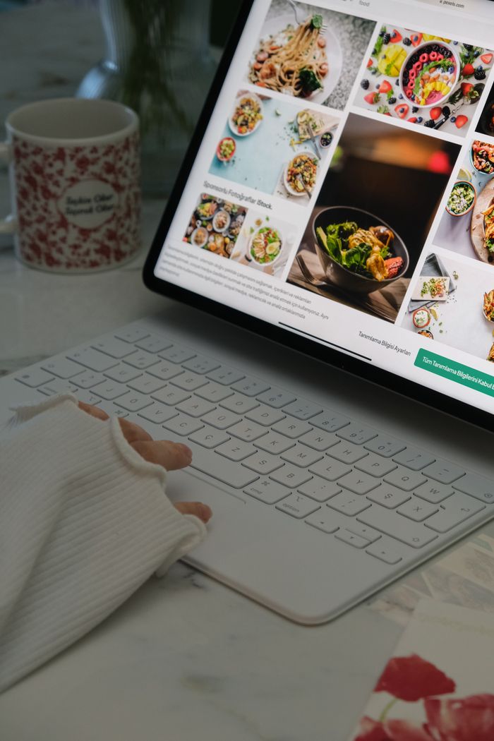 portfolio-01 A person uses a white laptop to browse food recipes, with a mug and cozy atmosphere.